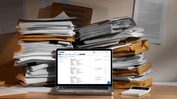 Notebook com o sistema McFile em meio a pilhas de documentos físicos, representando a digitalização e gestão documental na empresa.