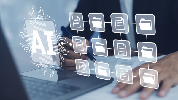 A professional's hands writing with a pen at a desk, next to a laptop, with a digital overlay of an "AI" chip connected by lines to a network of document and folder icons.