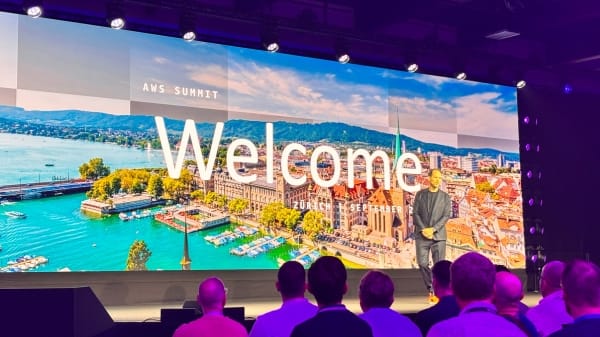 Telão de abertura do AWS Summit Zurique 2026, na Messe Zürich, com a palavra "Welcome" sobre uma vista panorâmica da cidade
