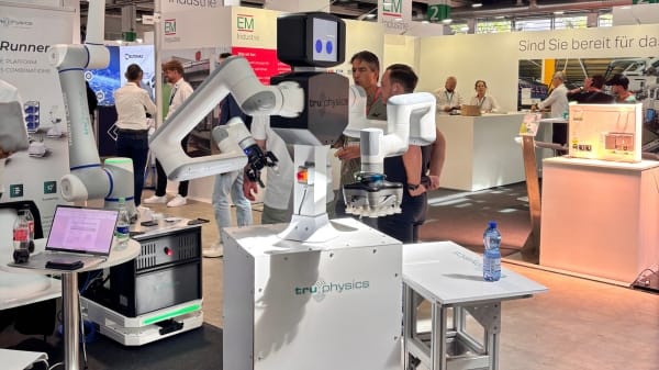 Foto de feira de automação industrial em Zurique com braços robóticos e equipamentos de robótica expostos em um estande, com visitantes ao fundo.